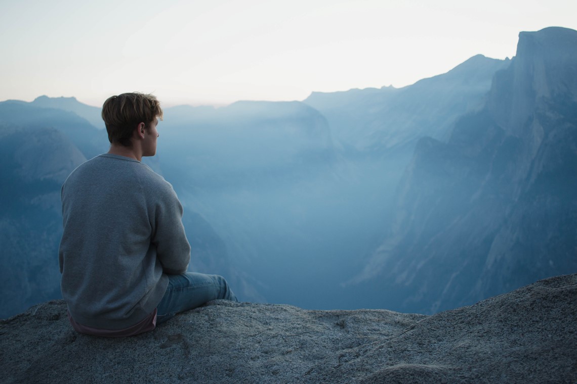 Person sitting on a cliff, looking at nature