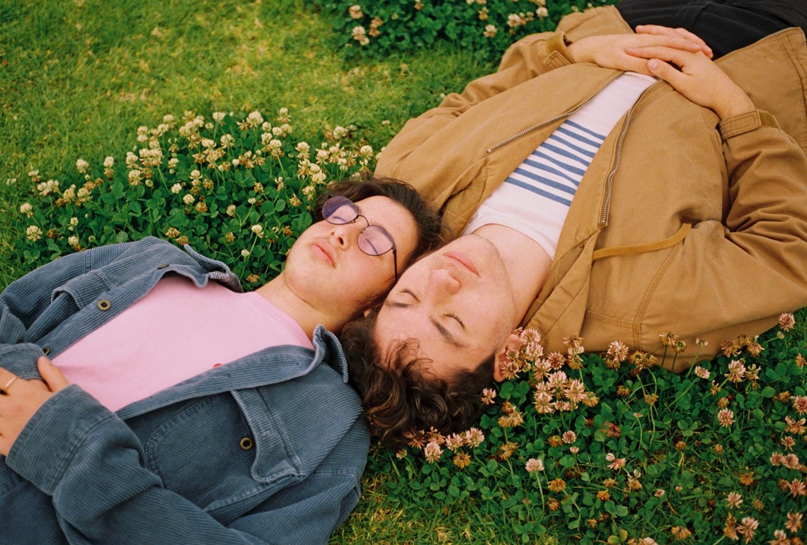 Two people laying on a grassy field with their eyes closed