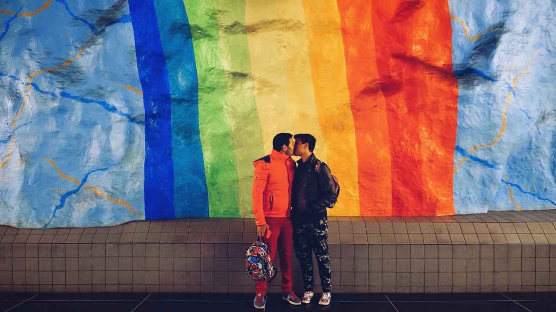 Two people kissing in front of the gay rainbow flag