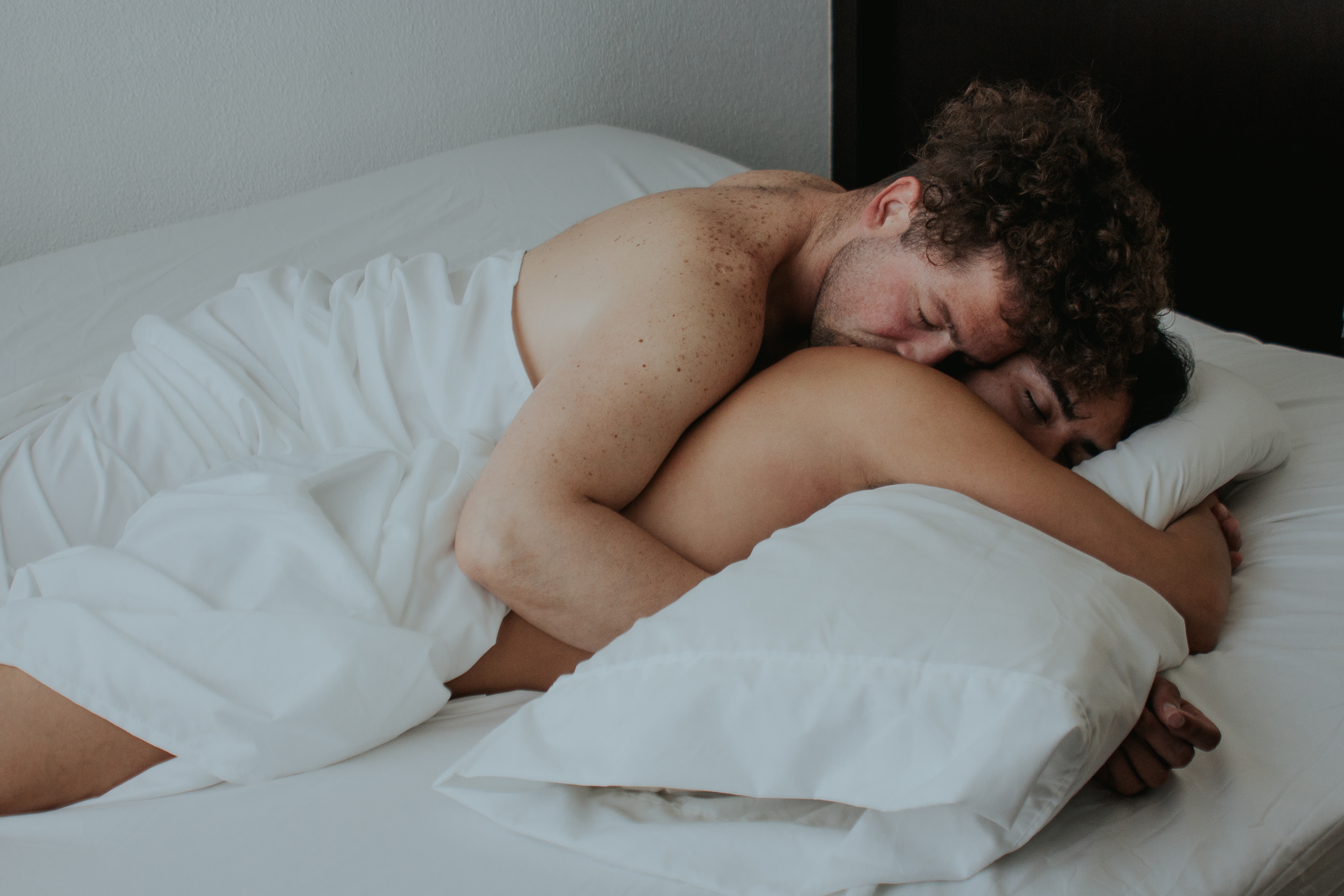Two people under the sheets cuddling in bed