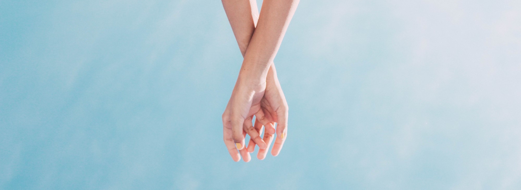 two hands meeting from above, with a sky background