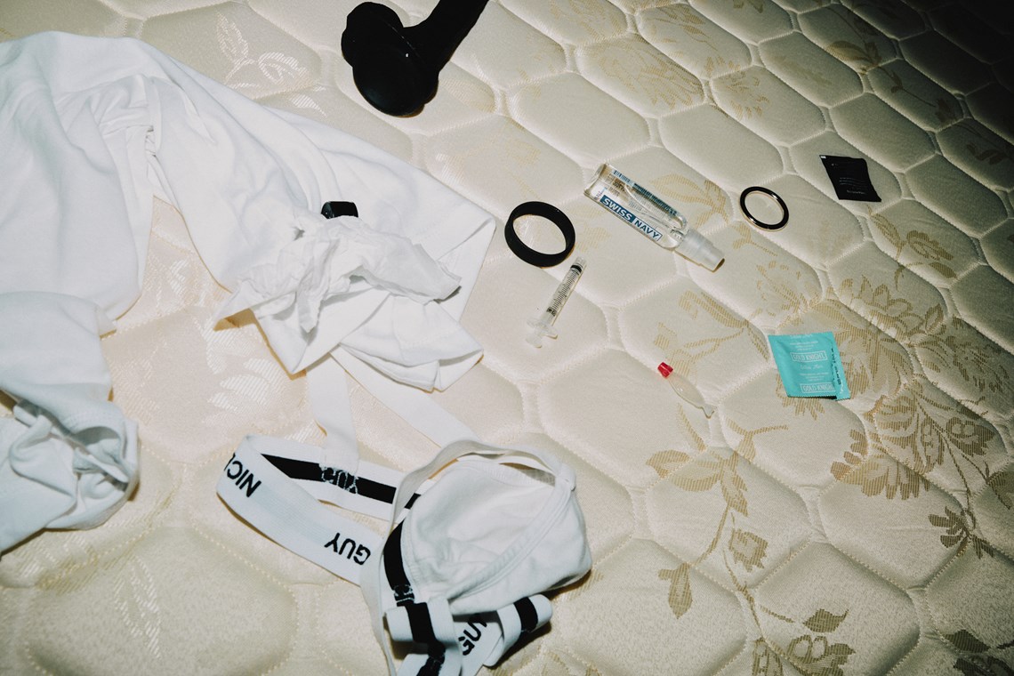 Drug and sex-related paraphernalia scattered across a bare mattress, including a jock strap, shirt, dildo, condom, lube, cock ring and syringe.